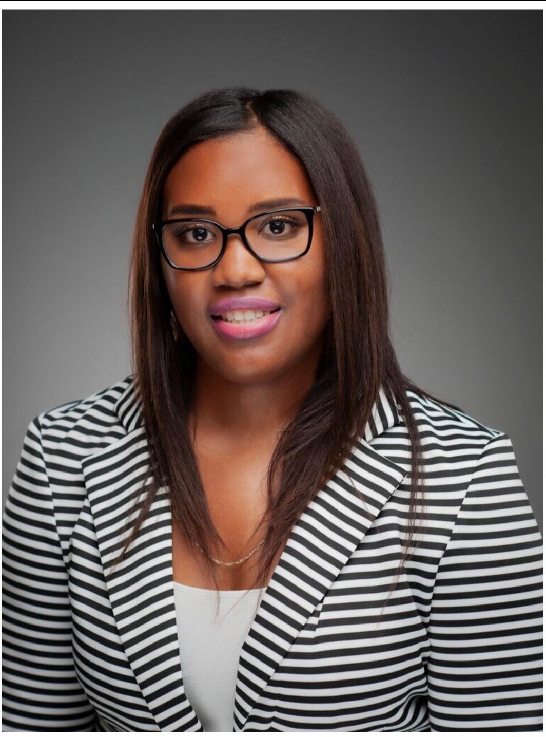 Professional headshot of a smiling woman with long dark hair, glasses, wearing a black and white striped blazer over a white top against a gray background